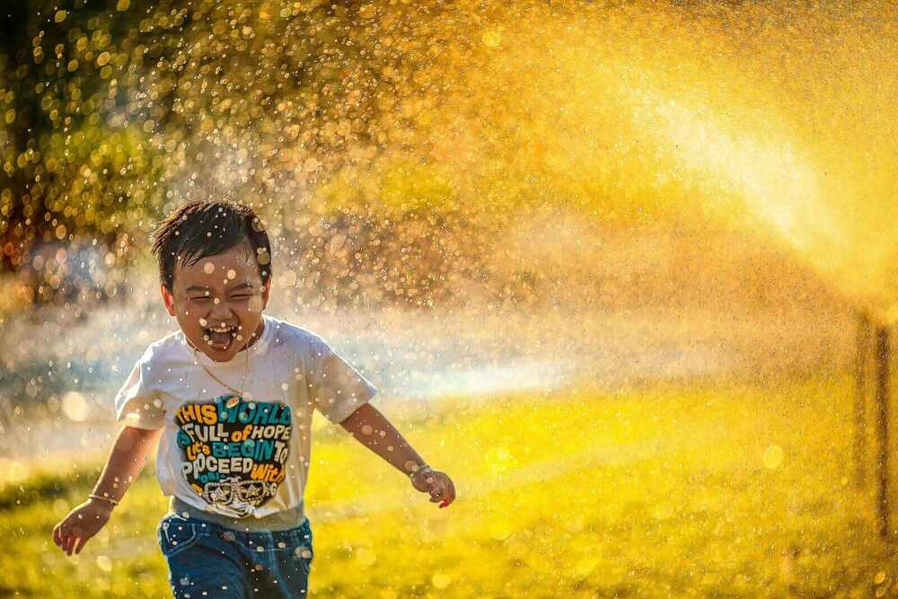 The image shows a laughing child in the rain